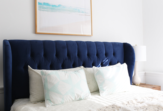 Blue tufted headboard with beach print above it